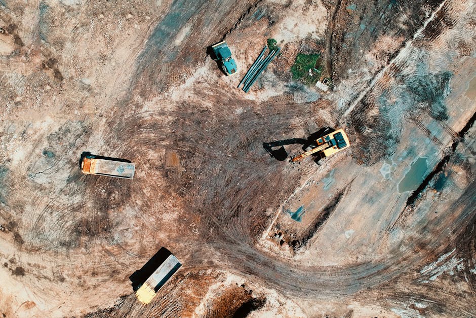 High-angle aerial view of construction site with earthmoving equipment and trucks.