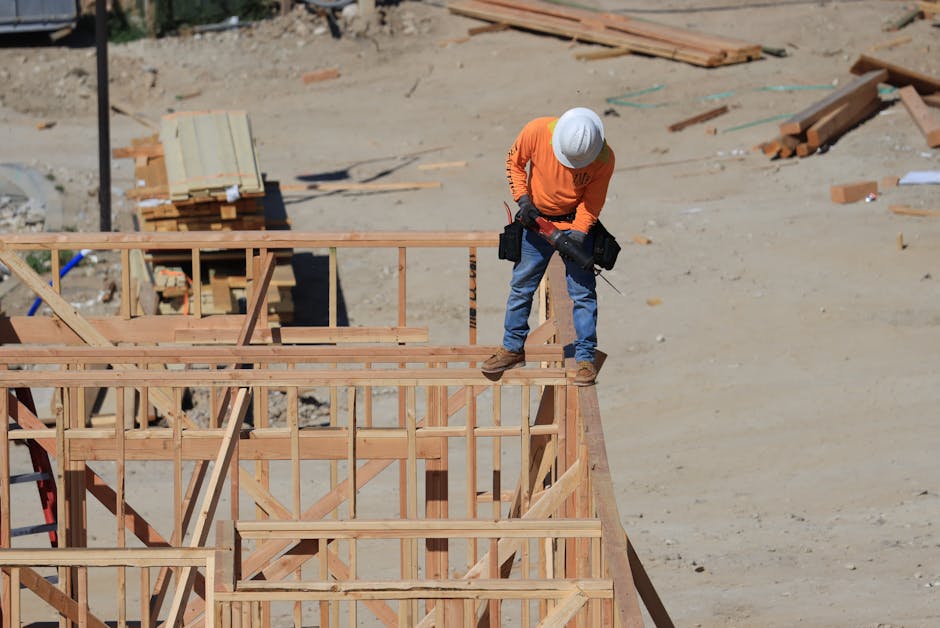 A construction worker wearing a safety helmet uses a drill on a wooden framework at a construction site